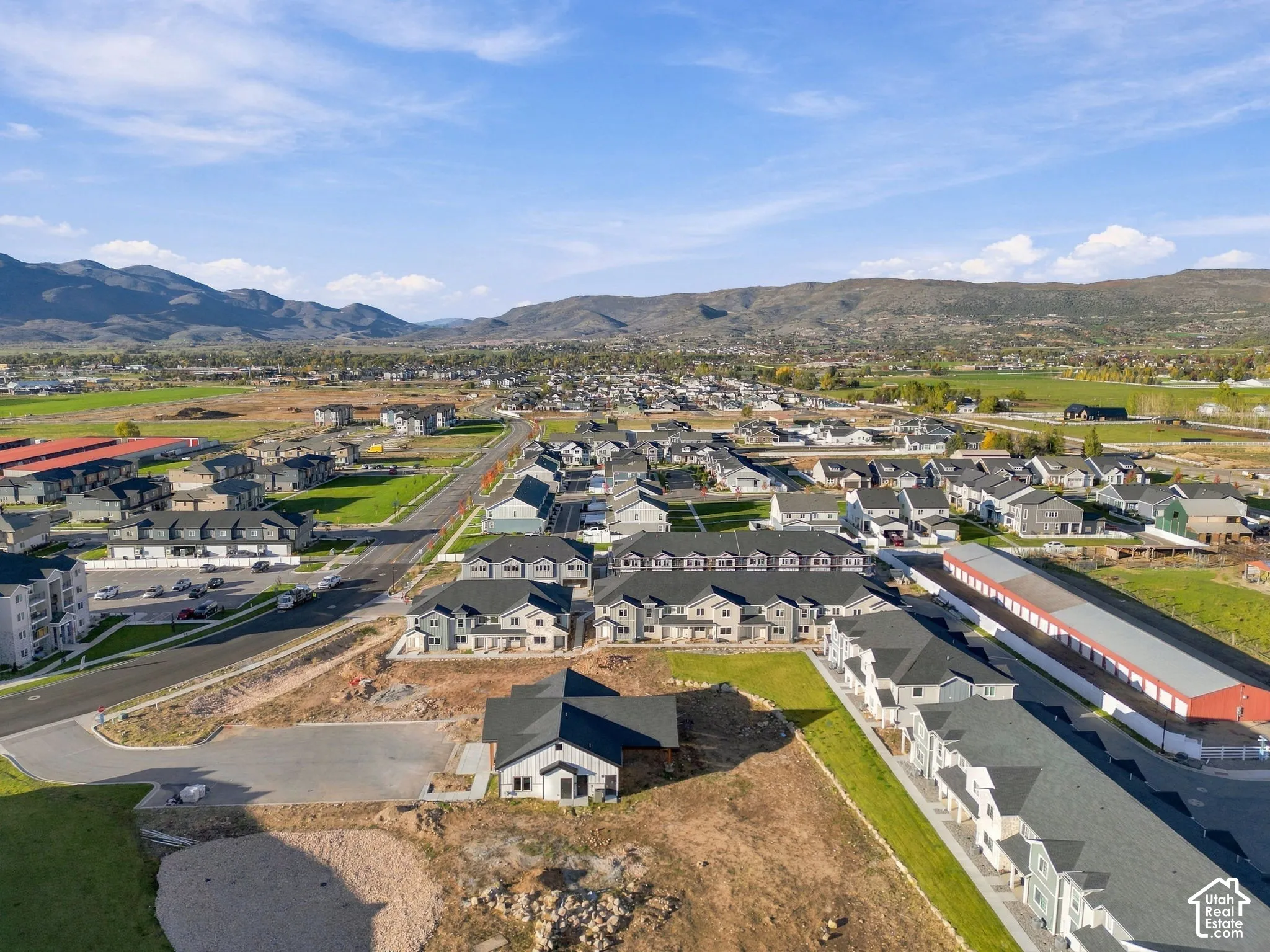 Aerial perspective of a multi-unit residential complex featuring asphalt shingle roofing, paved roadways, and mountain range backdrop