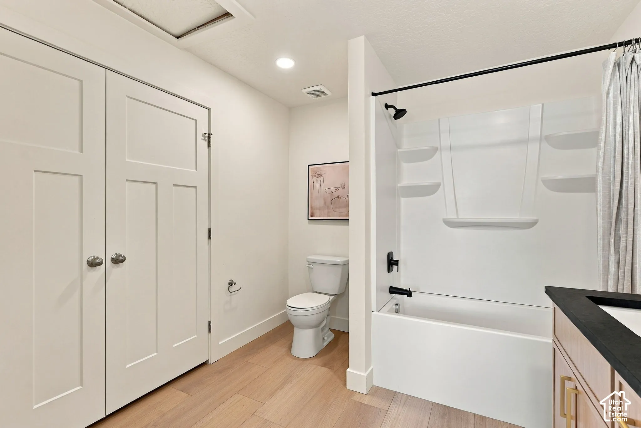 Bathroom featuring wood-finish flooring, a vanity with a dark countertop, a bathtub with an integrated shower surround, and shaker-style closet doors
