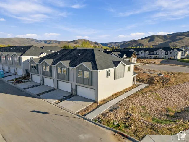 Multi-unit residential exterior featuring a light-colored facade, vertical paneling accents, asphalt shingle roofing, multi-car garages, and a mountainous backdrop