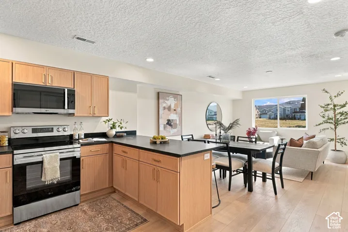Kitchen featuring light-finish cabinetry, dark solid-surface countertops, built-in stainless steel appliances, recessed ceiling lighting, and wide-plank wood-finish flooring
