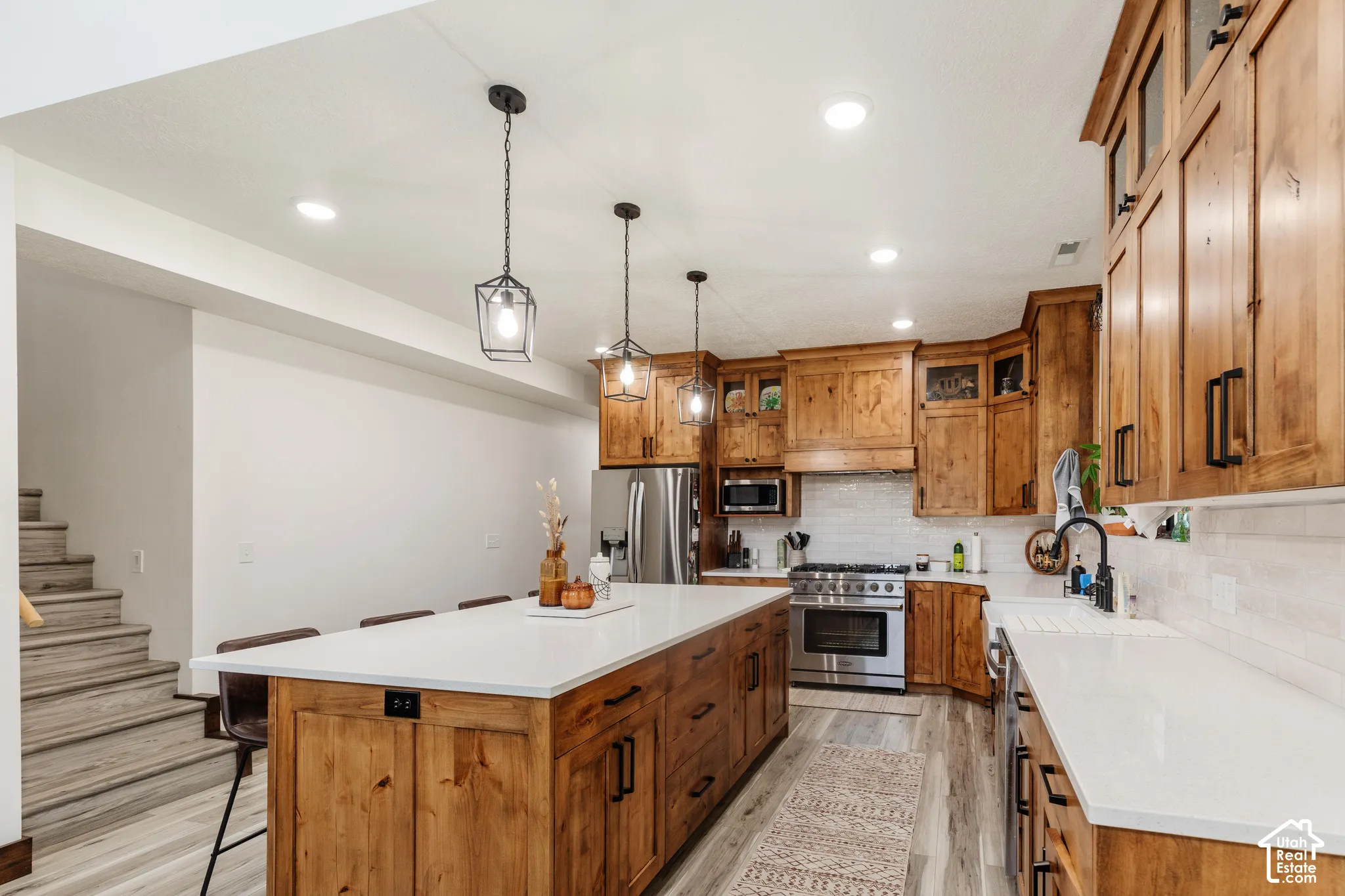 Kitchen featuring knotty wood cabinetry, quartz countertops, subway tile backsplash, stainless steel appliances, and three industrial-style pendant lights