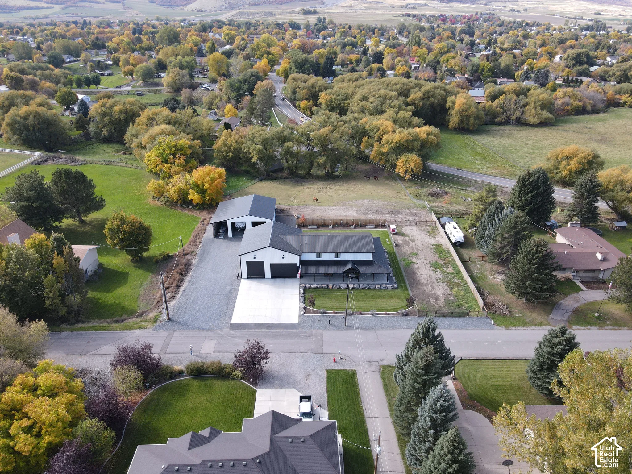 Aerial perspective of a property featuring a detached metal-sided workshop, a multi-bay attached garage, a concrete driveway, and a covered front porch
