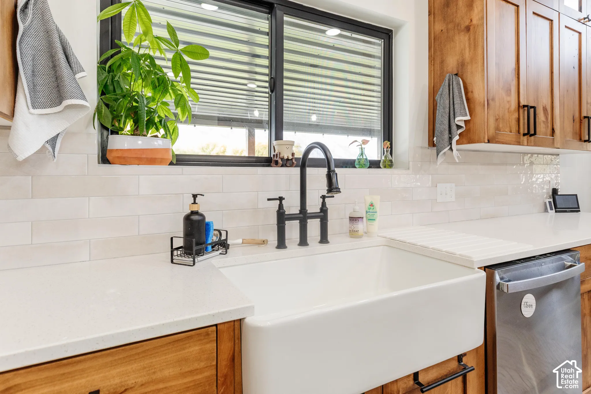 Farmhouse-style apron front sink, matte black gooseneck faucet, light-toned linear backsplash tile, solid-surface countertops, and wood-finish cabinetry with dark hardware