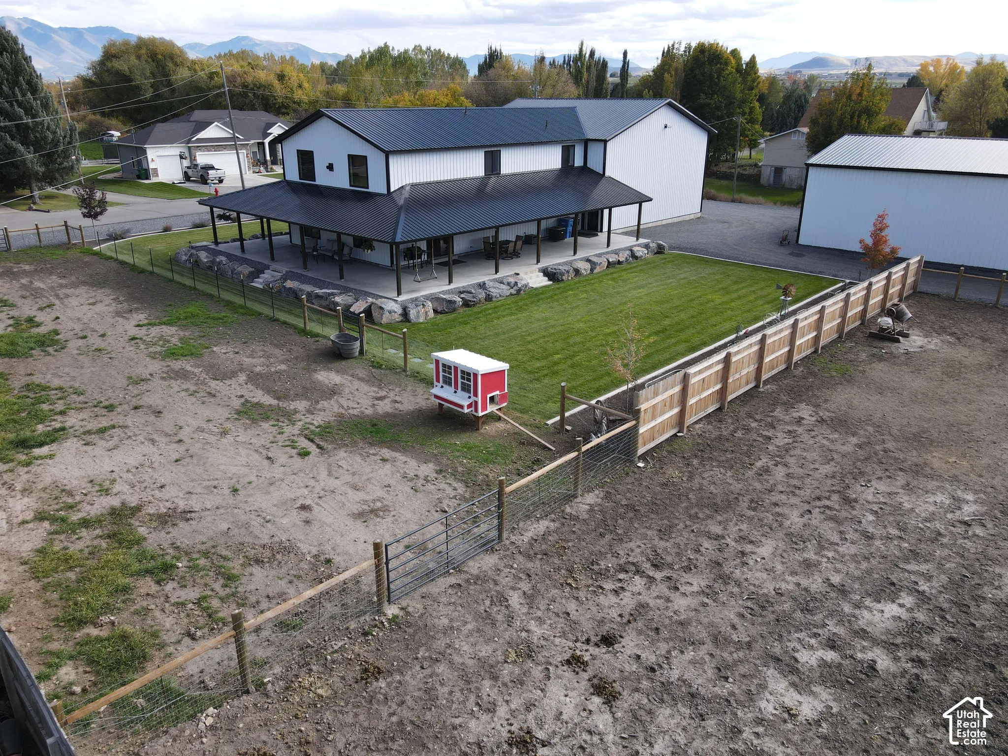 Two-story residence featuring a metal roof, expansive covered wrap-around porch, boulder retaining wall, manicured lawn, and perimeter wood and wire fencing
