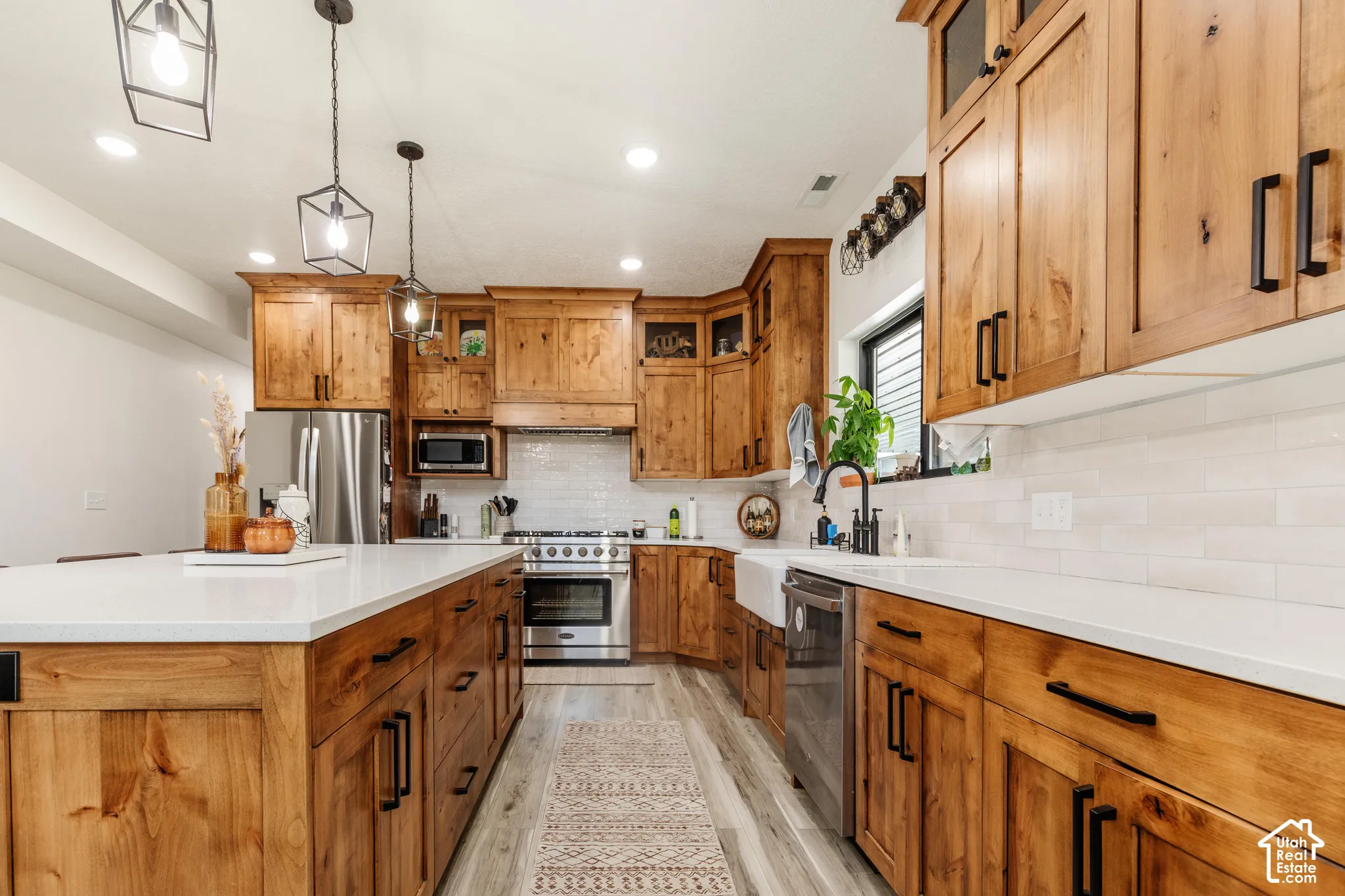 Kitchen featuring wood cabinetry, stone countertops, a farmhouse-style sink, stainless steel appliances, and matte black hardware