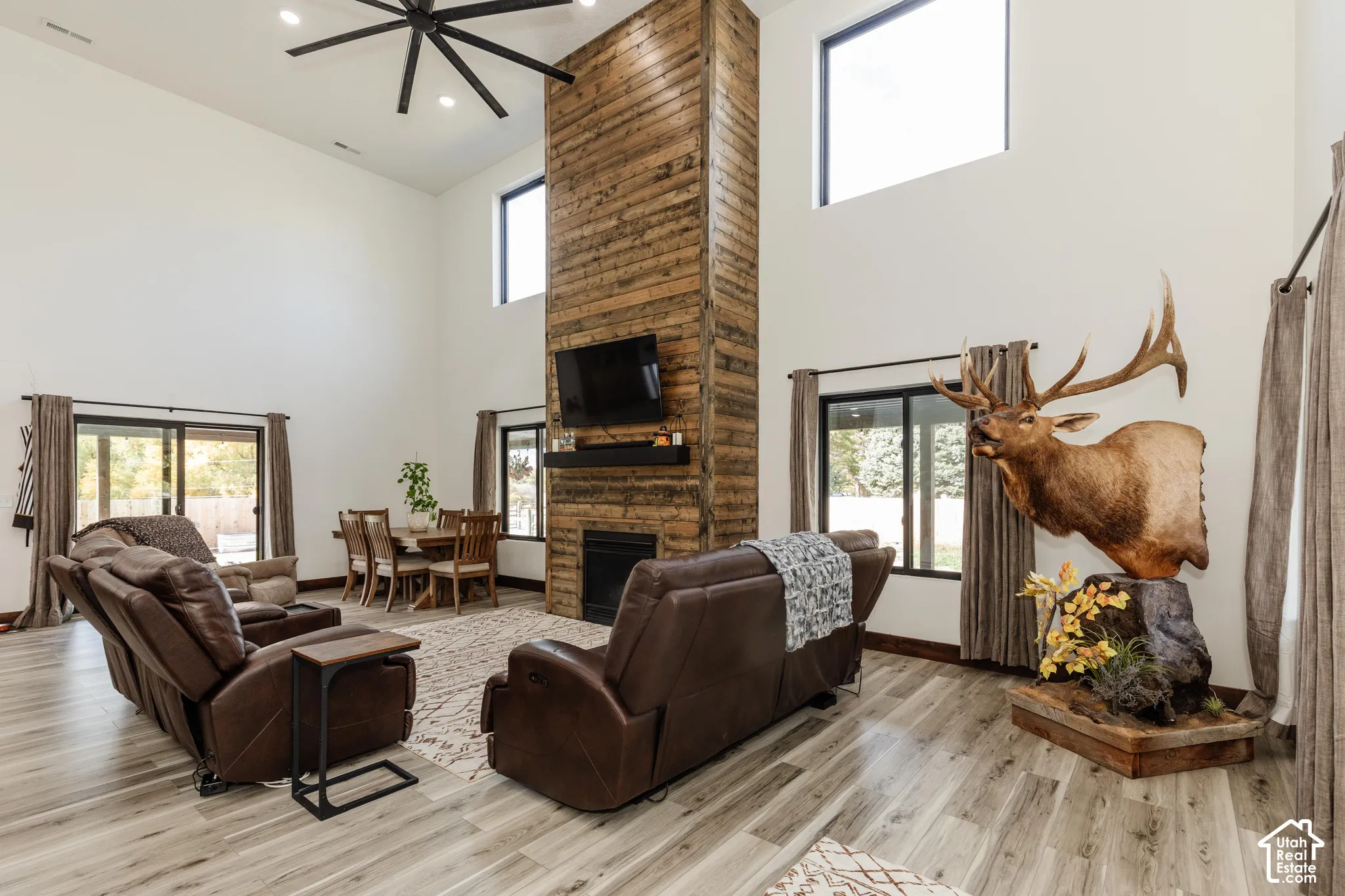 Double-height ceiling, floor-to-ceiling wood-paneled fireplace, wood-finish flooring, recessed lighting, and large multi-pane windows