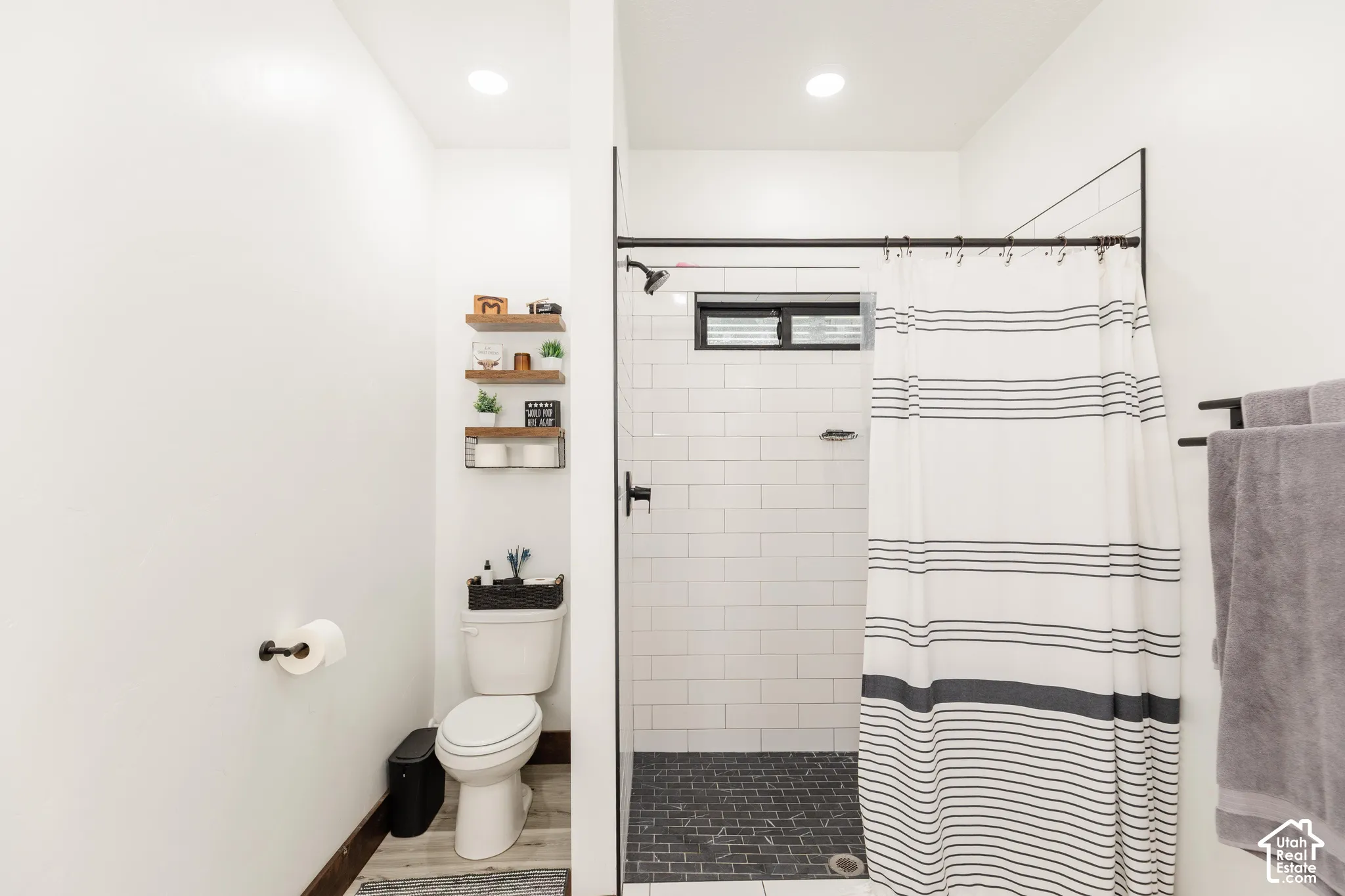 Walk-in shower with white subway tile, dark stone-finish flooring, matte black fixtures, recessed lighting, and built-in wall shelving