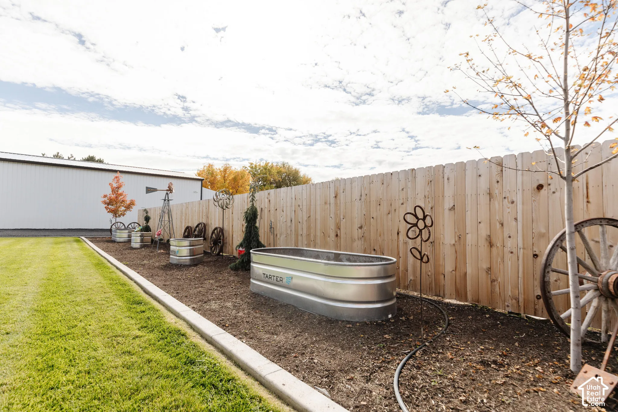 Manicured lawn bordered by concrete edging, metal stock tank garden beds, and wood privacy fencing