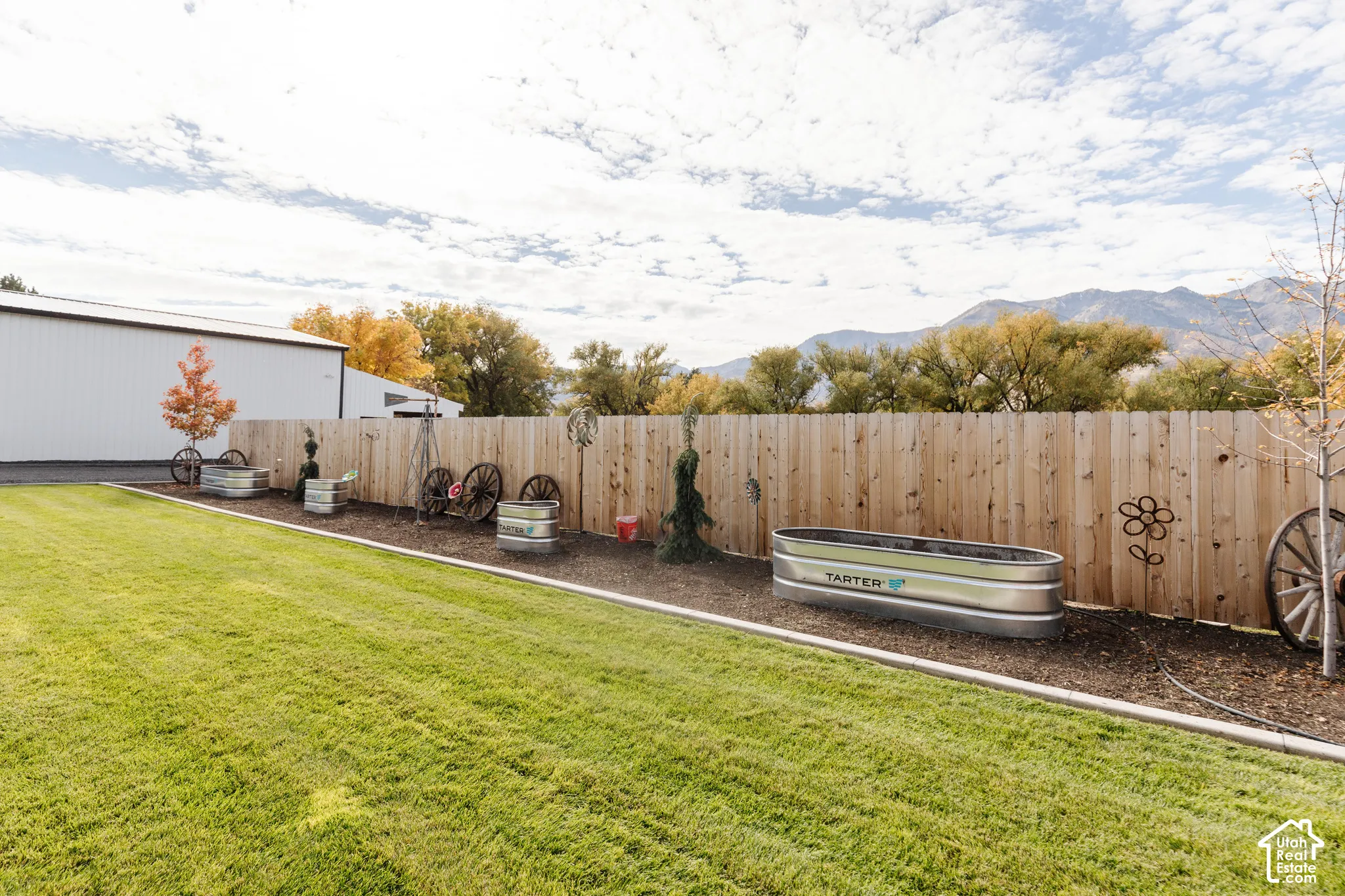 Backyard featuring a manicured lawn, wood-panel fencing, metal raised garden beds, and mountain range scenery