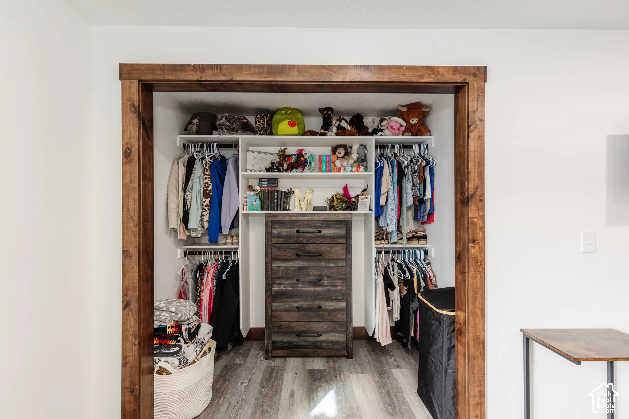 Reach-in closet featuring custom white built-in shelving, a centrally located integrated five-drawer dresser, and natural wood-finish trim casing