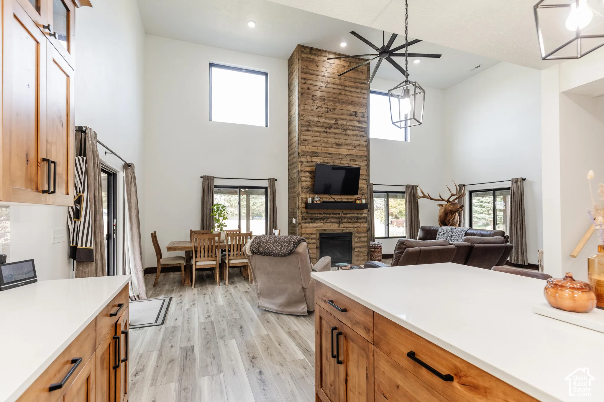 Vaulted ceiling living area featuring a full-height wood-clad fireplace, light-toned wood-finish flooring, recessed lighting, and a modern industrial-style pendant fixture