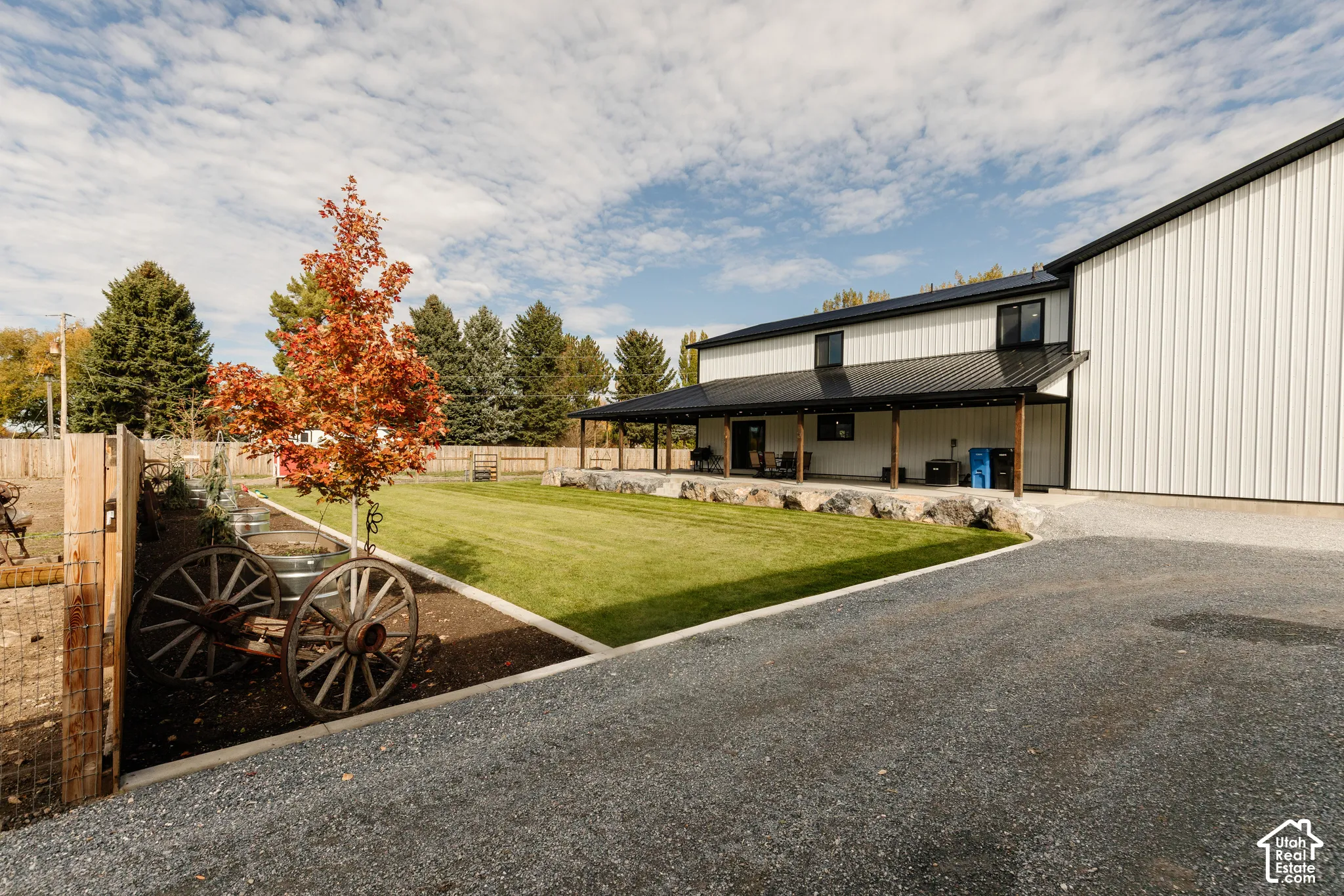 Expansive lawn bordered by stone retaining walls, covered patio, metal exterior siding, and gravel driveway