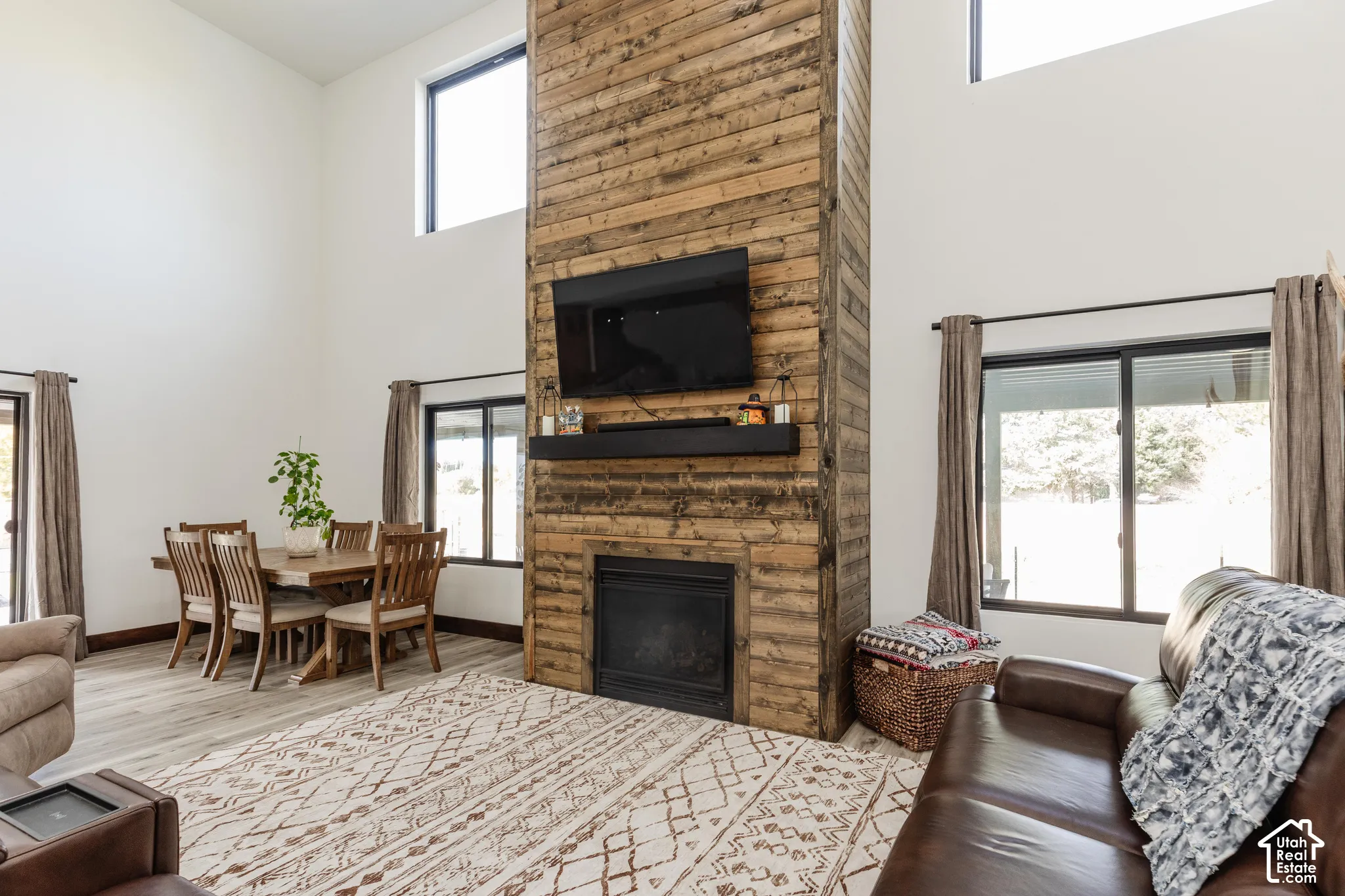 Double-height ceiling, floor-to-ceiling wood-plank fireplace surround, built-in black mantel, and wood-finish flooring