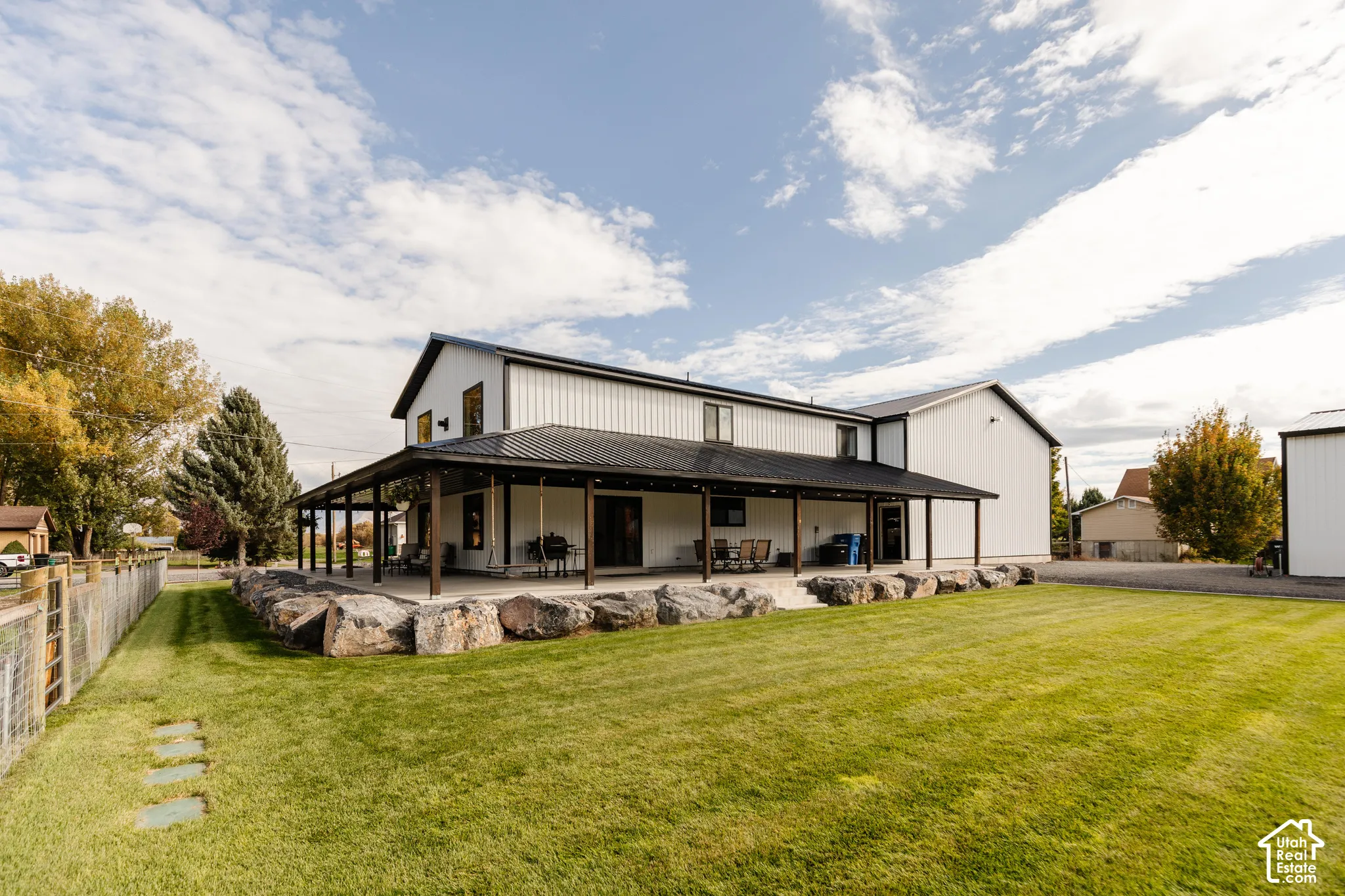 Metal-sided exterior with a standing seam metal roof and a full-length covered porch featuring timber posts and a concrete slab foundation bordered by stacked natural boulder landscaping