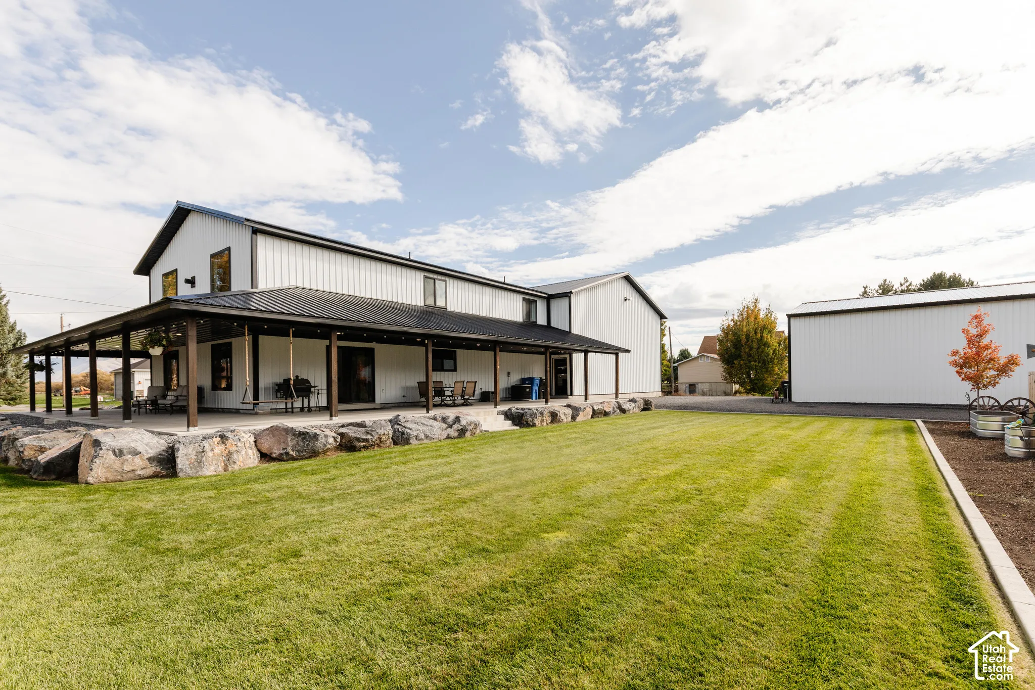 Exterior featuring vertical siding, metal roofing, expansive covered patio, natural stone hardscaping, and detached garage