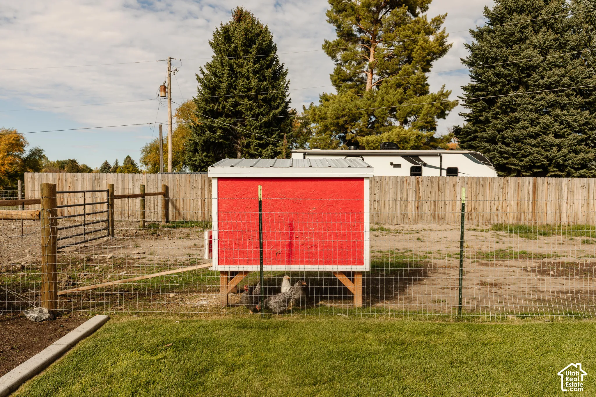 Enclosed outdoor structure with a red exterior and metal roof, positioned within a fenced area featuring wire perimeter security