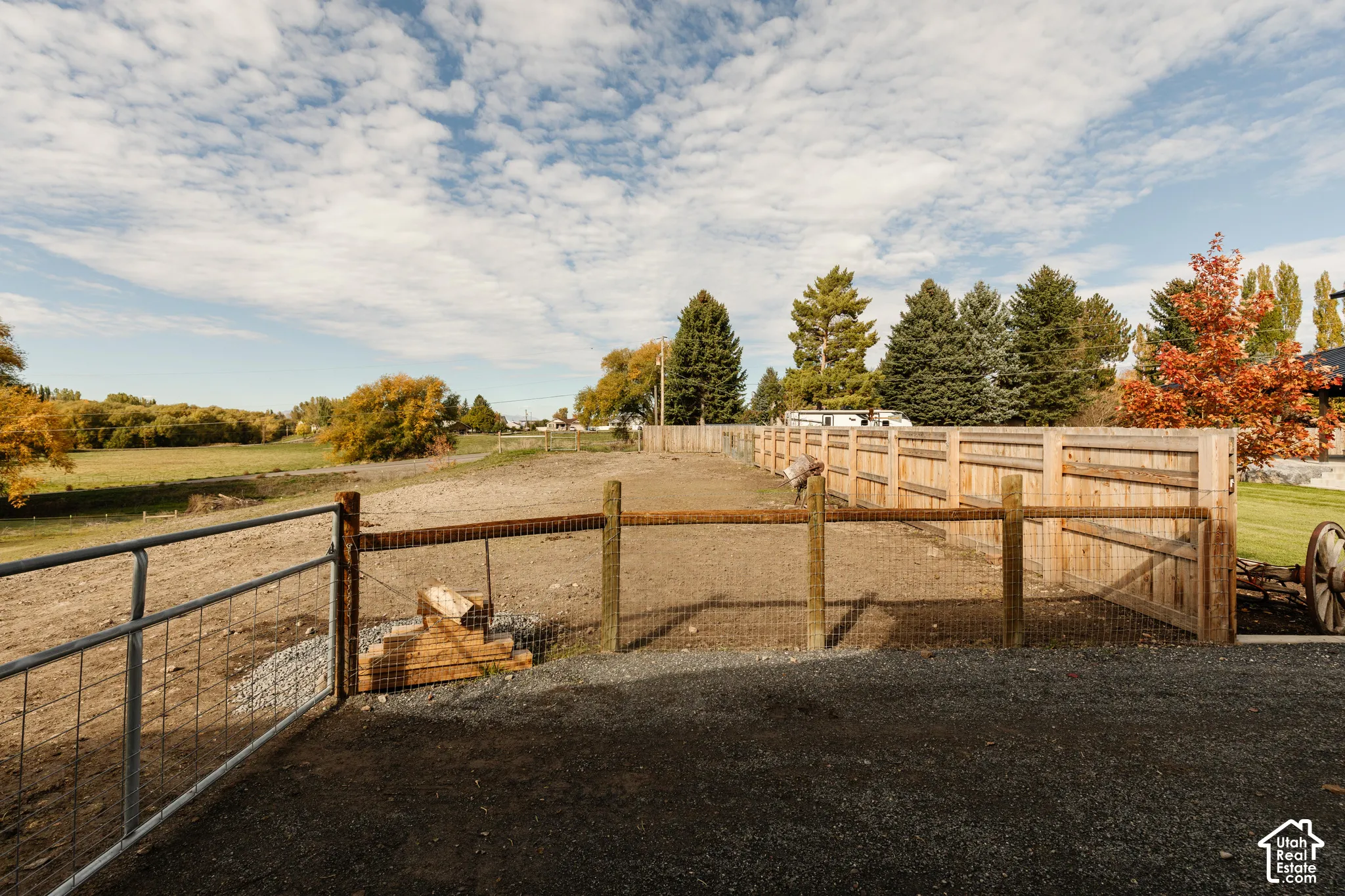 Expansive lot featuring horizontal wood fencing, wire mesh perimeter enclosures, metal gate, and gravel ground surfacing