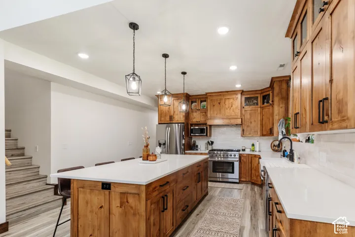 Kitchen featuring knotty wood cabinetry, quartz countertops, subway tile backsplash, stainless steel appliances, and three industrial-style pendant lights