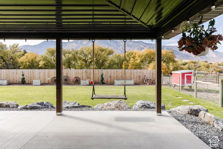Covered patio featuring a concrete floor, mountain scenery, manicured lawn, natural boulder edging, and perimeter wood fencing