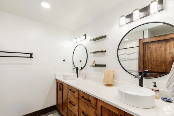 Dual-sink vanity featuring wood cabinetry, white stone countertops, fluted vessel sinks, matte black fixtures, and circular mirrors