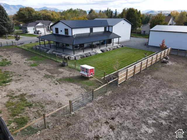 Two-story residence featuring a metal roof, expansive covered wrap-around porch, boulder retaining wall, manicured lawn, and perimeter wood and wire fencing