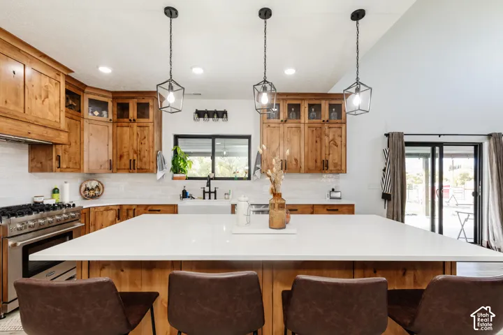 Kitchen featuring stained wood cabinetry, quartz countertops, oversized center island, stainless steel gas range, and geometric pendant lighting