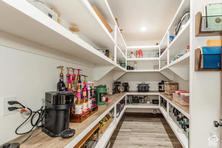 Walk-in pantry featuring U-shaped white built-in shelving, wood-finish countertops, and wood-finish flooring