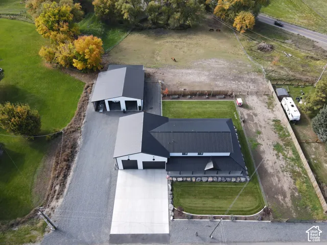 Aerial perspective of property featuring a multi-structure layout with metal roofing, a detached garage, expansive lawn areas, concrete driveways, and stone retaining walls