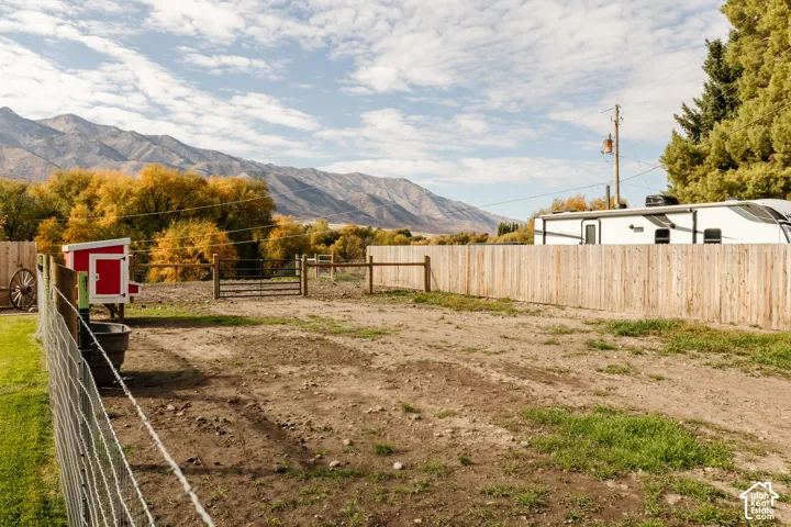 Fenced outdoor area featuring a wood-rail perimeter, wire mesh enclosure, built-in coop, and mountain backdrop