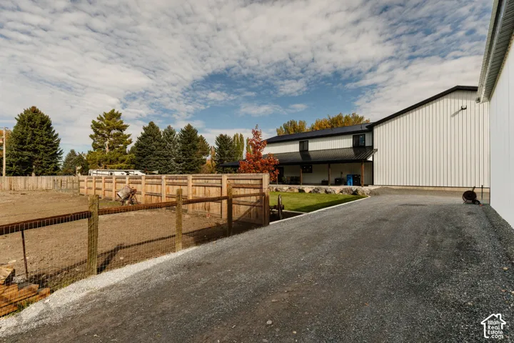 Exterior featuring a metal-sided building with a covered porch, a gravel driveway, wood and wire fencing, and a manicured lawn