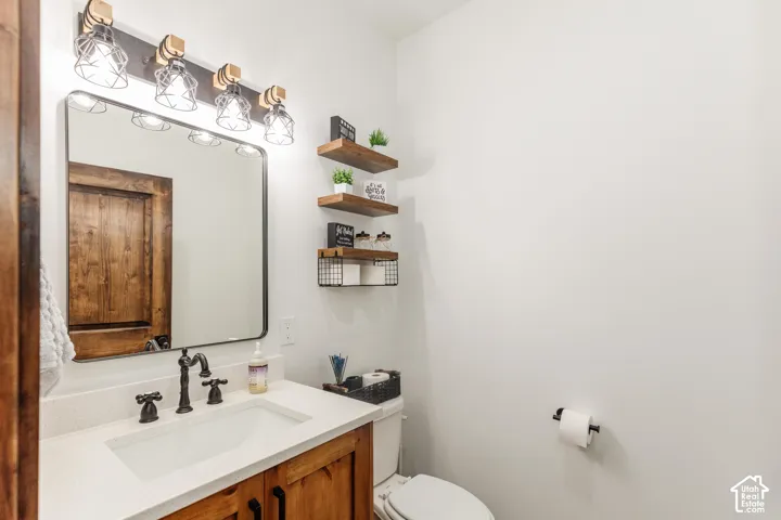 Bathroom featuring a vanity with a light-toned countertop, custom wood-finish cabinetry, a rectangular mirror with a metal frame, oil-rubbed bronze plumbing fixtures, and integrated wood shelving
