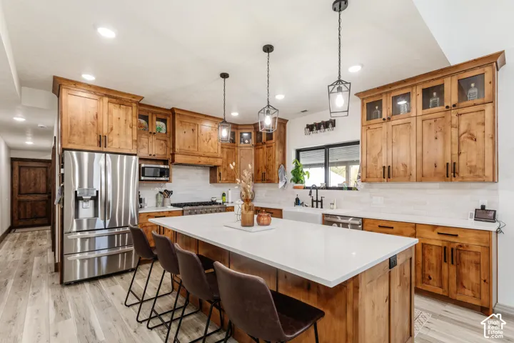 Kitchen featuring natural wood cabinetry, quartz countertops, a central island, recessed lighting with three geometric pendant fixtures, and wood-finish flooring