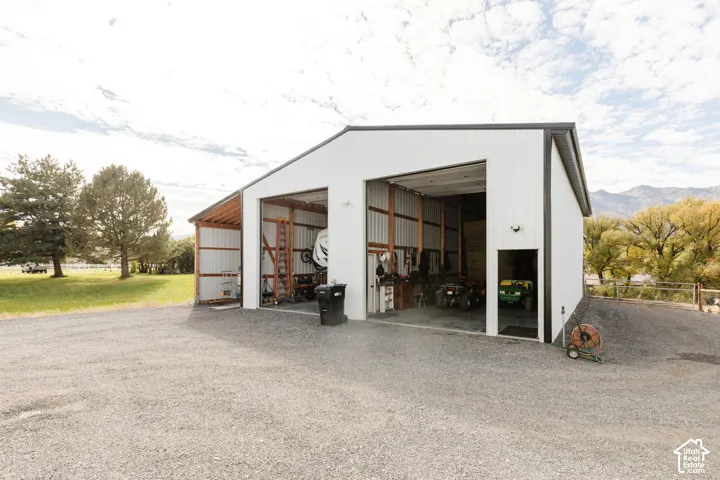 Metal-clad detached workshop featuring three high-clearance bays, exposed structural framing, and gravel driveway access