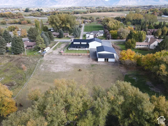 Aerial perspective of property featuring a multi-structure footprint, expansive acreage, fenced pasture, metal-roofed workshop, and a backdrop of mountain scenery