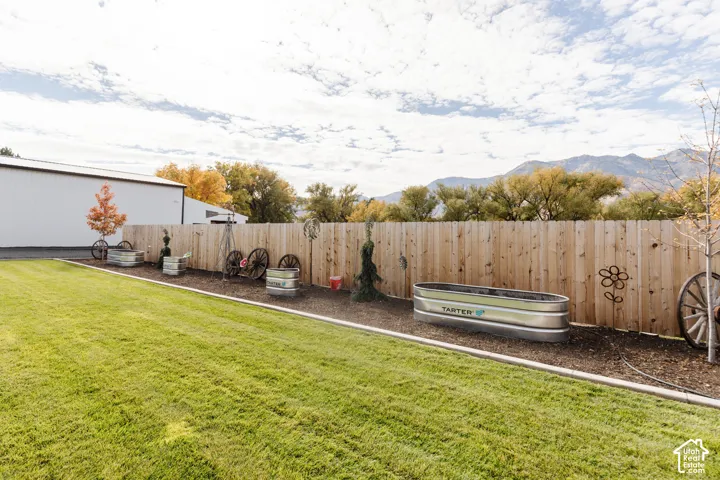 Backyard featuring a manicured lawn, wood-panel fencing, metal raised garden beds, and mountain range scenery