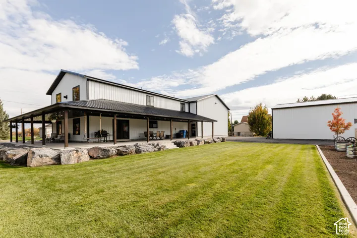 Exterior featuring vertical siding, metal roofing, expansive covered patio, natural stone hardscaping, and detached garage