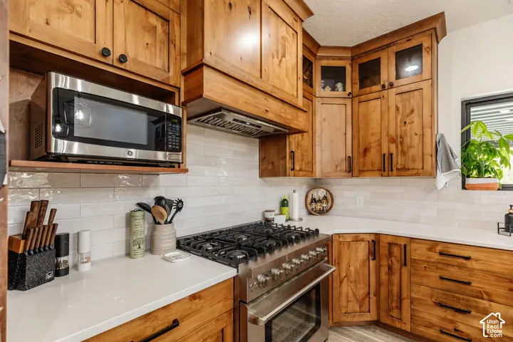Custom stained wood cabinetry, stainless steel gas range, built-in microwave, subway tile backsplash, and quartz countertops