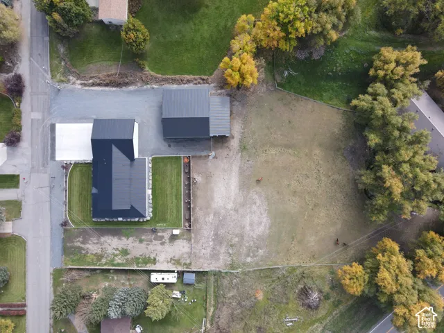 Aerial view featuring a multi-structure property with metal roofing, a detached garage, expansive open grounds, and established trees