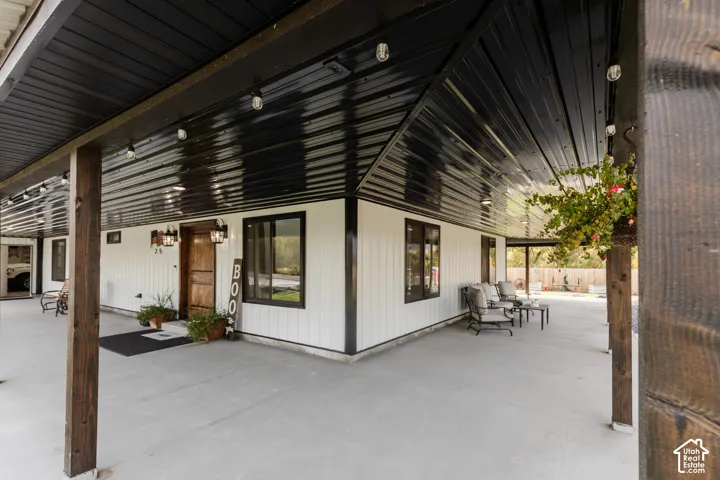 Covered wrap-around porch featuring white board-and-batten siding, a black corrugated metal ceiling, exposed wood support posts, and black exterior light fixtures