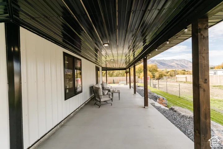 Covered porch featuring concrete flooring, exposed wood support posts, corrugated metal ceiling, and vertical metal siding, set against a mountain backdrop