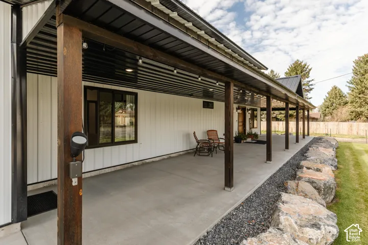 Covered concrete patio featuring vertical siding, metal roofing, wood support posts, and a decorative boulder landscape border