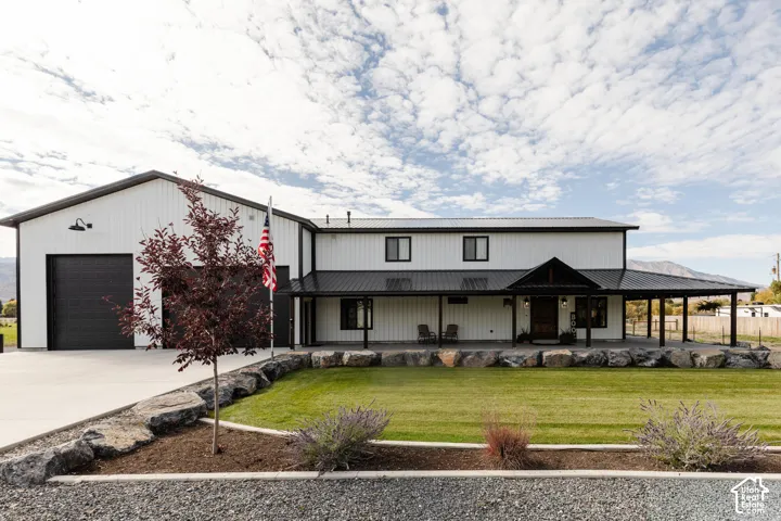 Modern white vertical-siding exterior featuring a metal roof, expansive covered porch, large integrated garage, and decorative stone landscaping border