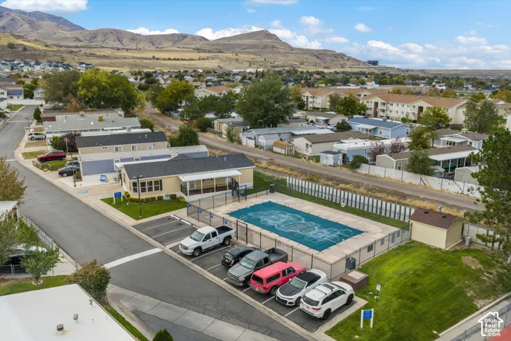 Aerial perspective featuring a fenced swimming pool with a safety cover, dedicated surface parking stalls, manicured lawn areas, and prominent mountain backdrop