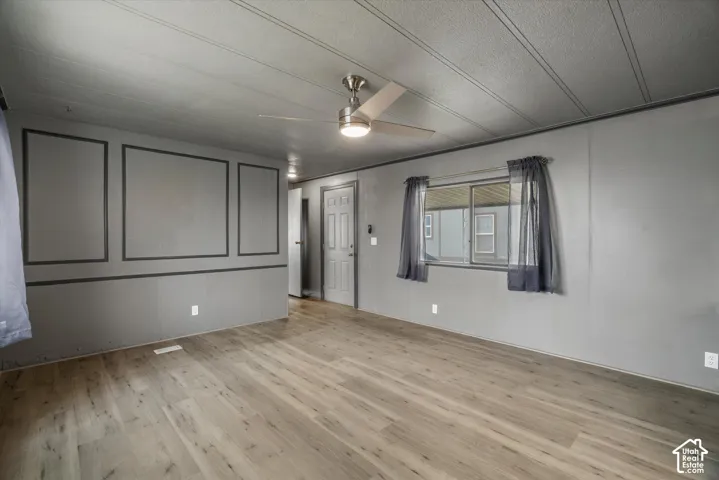 Interior space featuring wood-finish flooring, decorative wall molding, a brushed-metal ceiling fan with integrated lighting, and a multi-panel door