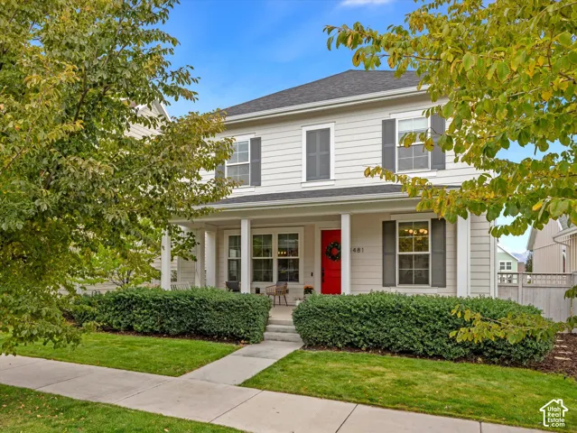 Two-story residence featuring light-toned horizontal siding, dark grey window shutters, a covered front porch with square columns, and a concrete walkway