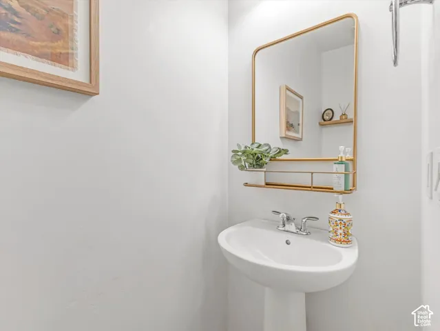 Half-bathroom featuring all-mounted gold-toned mirror with integrated shelving, white porcelain pedestal sink, and dual-handle chrome faucet