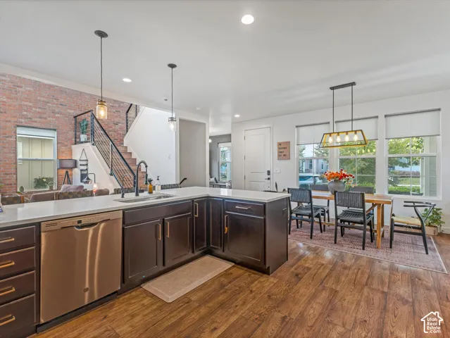 Kitchen featuring dark cabinetry, quartz countertops, stainless steel appliances, wood-finish flooring, and a decorative brick wall