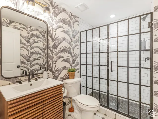 Slatted wood-finish vanity with a rectangular sink, wall-mounted matte black faucet, framed mirror, and a walk-in shower featuring a grid-patterned glass enclosure with white subway tile surround and hexagonal floor tile