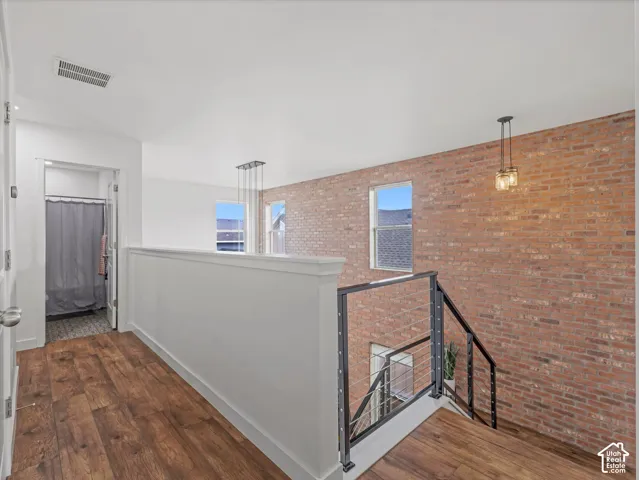 Exposed brick feature wall with industrial-style cable railing, wood-finish flooring, and multi-light pendant fixtures