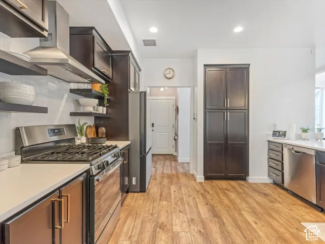 Kitchen featuring dark-finish cabinetry, stainless steel appliances, wood-finish flooring, quartz countertops, and a subway tile backsplash